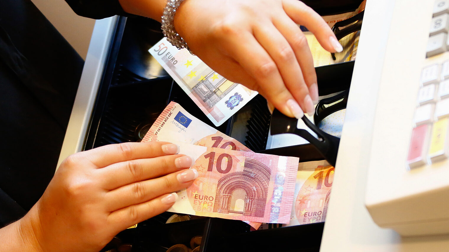 Nahaufnahme zweier Hände die Geld in eine Kasse einsortieren