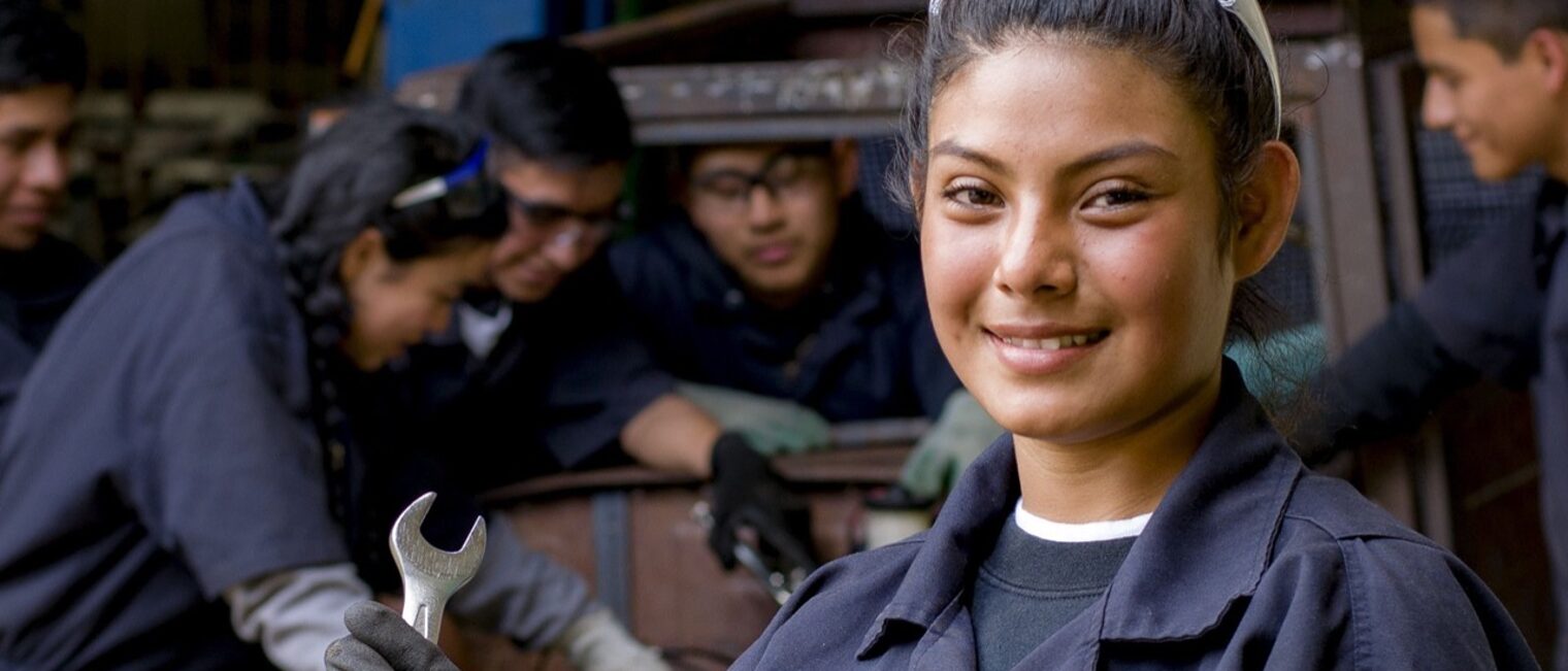 Junge Nepalesin in KFZ-Betrieb Eine junge Nepalesin im Blaumann steht vor Gruppe junger Leute, die ein Auto reparieren