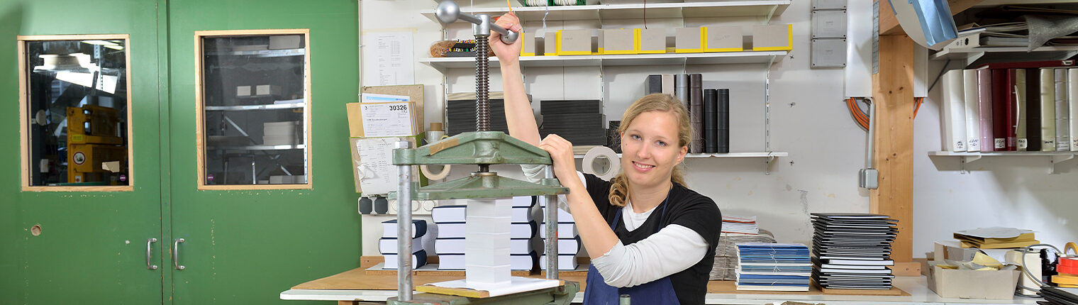 Buchbinderin in Werkstatt an einer Presse