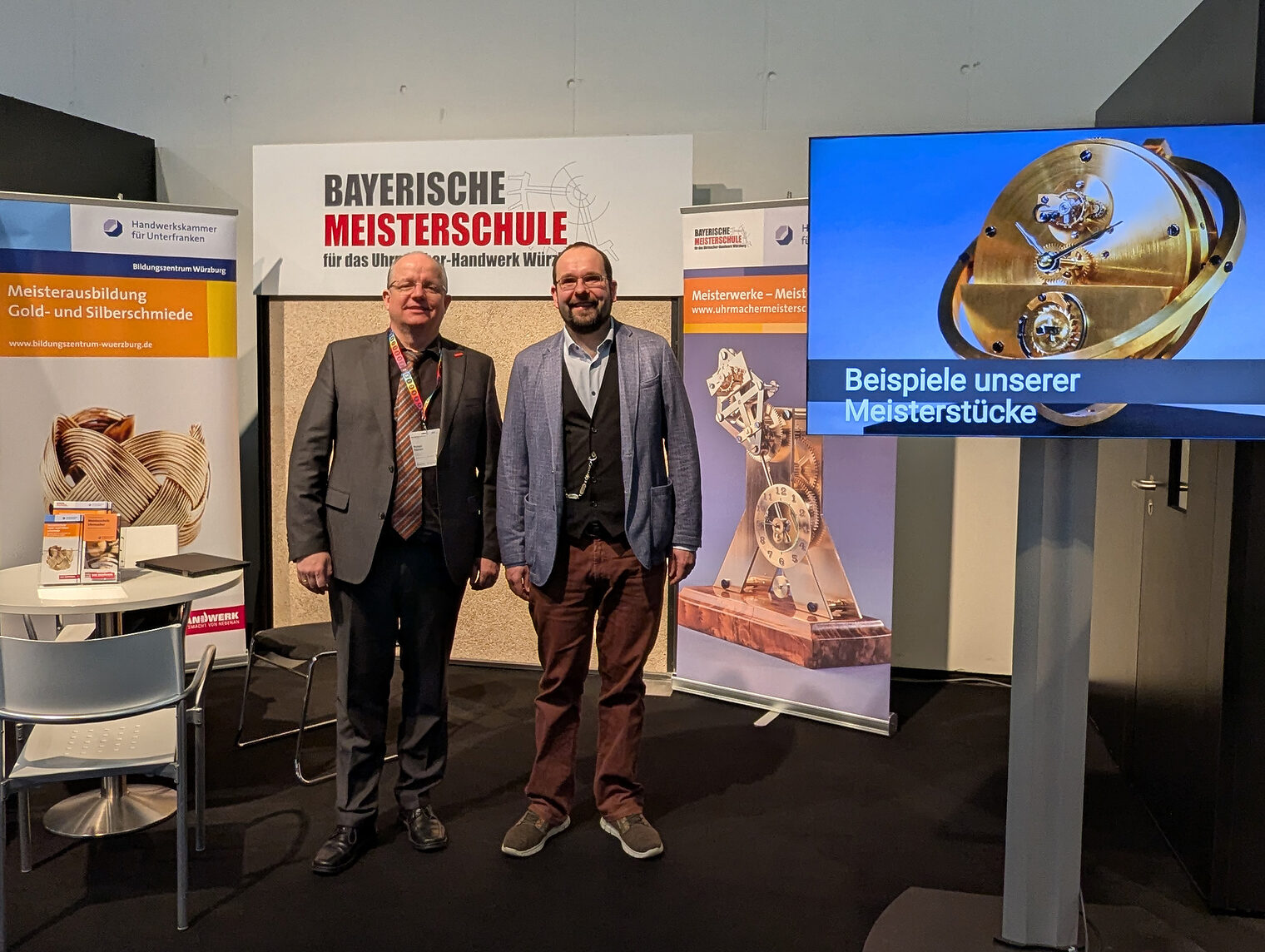 Herr Eberlein und Herr Philipp, Obermeister in Mittelfranken, stehen vor dem Stand der Bayerischen Uhrmachermeisterschule.
