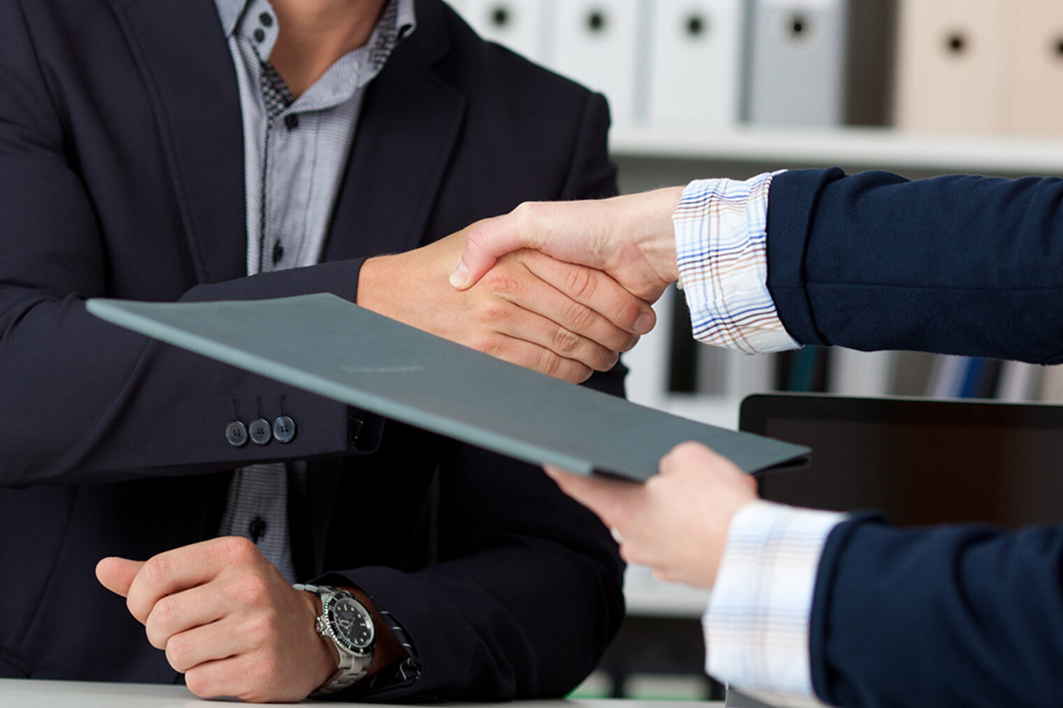 Handschlag | Gespräch Zwei Personen mit Hemd und Anzug sitzen an Schreibtisch und reichen sich die Hand und übergeben Unterlagen