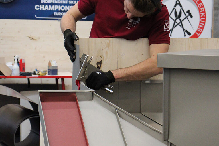 Spengler arbeitet an Blech an einem Dachmodell