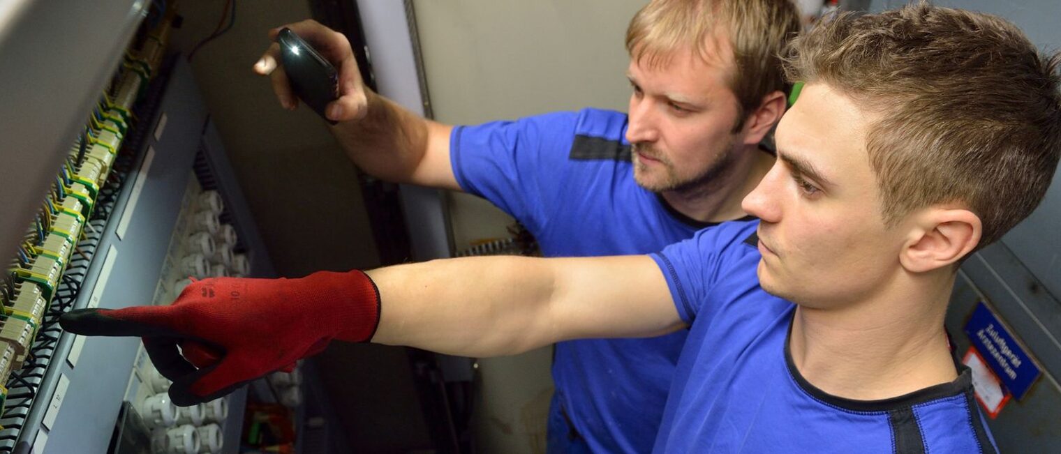 Ein junger Mann mit blauem Oberteil zeigt mit dem Finger auf diverse Schalter